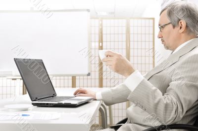 Portrait of an older businessman with a computer and a cup.