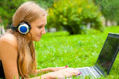 A smiling young girl with laptop outdoors listening music by hea