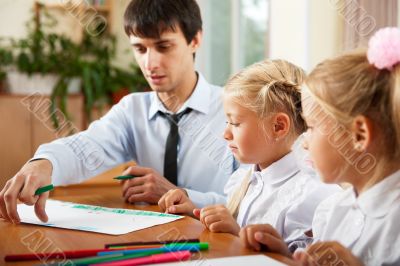 Teacher helping students with schoolwork in school classroom. Ho