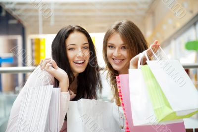 Two excited shopping woman together inside shopping mall. Horizo