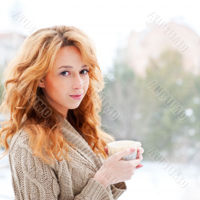 Portrait of beautiful red hair girl drinking coffee on winter ba