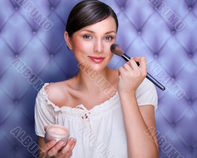 Portrait of attractive young adult woman applying blusher agains