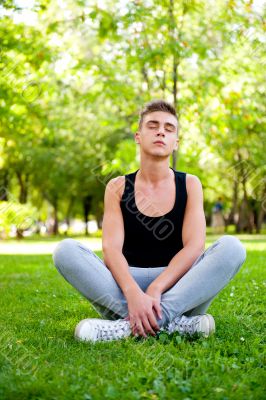 Beautiful young man in meditation pose outdoors.