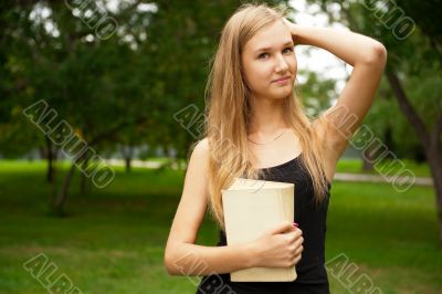 Beautiful female student outdoors with a book at campus park