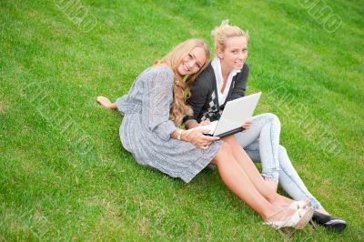 Portrait of two smiling women using laptop on a green meadow at 