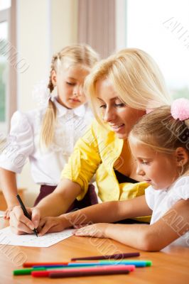 Young pretty teacher helping her little students in classroom