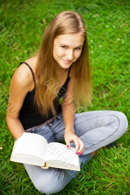 Beautiful female student outdoors with a book at campus park