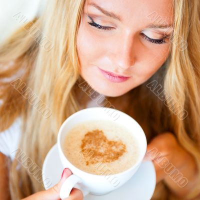Smiling woman drinking a coffee lying on a be