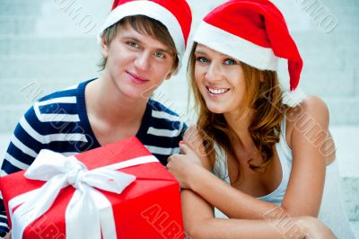 Young happy couple in Christmas hats standing together and holdi