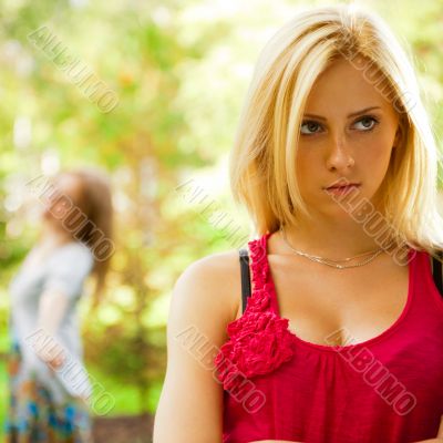 Upset teenage girl being jeered by group of the other young peop