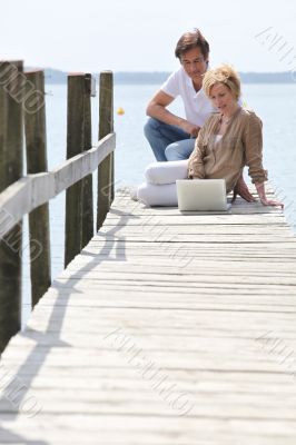 mature couple with laptop seated on pontoon