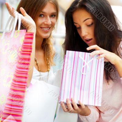 Two excited shopping woman resting on bench a