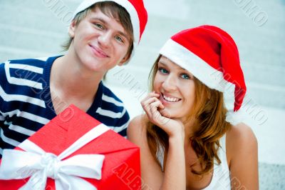 Young happy couple in Christmas hats standing together and holdi