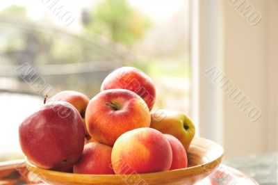 Closeup photo of red apples on wooden plate indoor against wide 