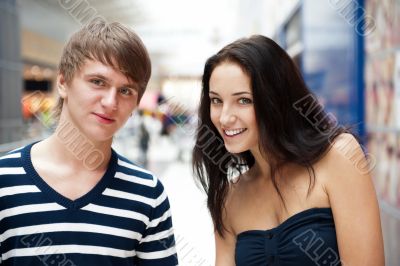 Portrait of young couple embracing at shopping mall and looking 