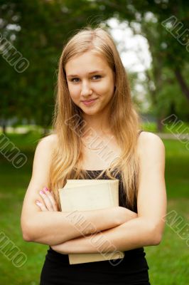 Beautiful female student outdoors with a book at campus park