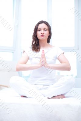 Young woman meditating with closed eyes in bright bedroom sittin