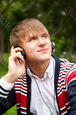 Student outside sitting on green grass and listening music via h