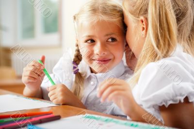 Two little girls gossip in classroom