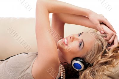 Young Girl enjoys listening music in headphones lying on sofa