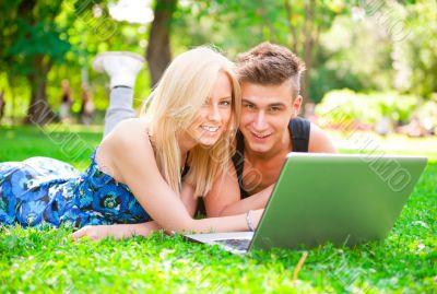 Portrait of young couple outdoor resting on green grass and usin
