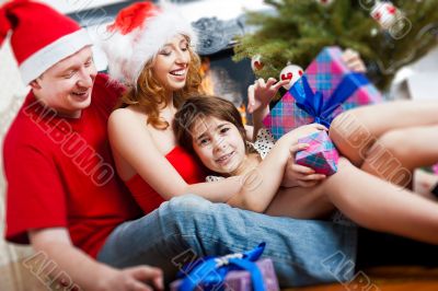 Young happy familye near a Christmas tree at home holding gift a