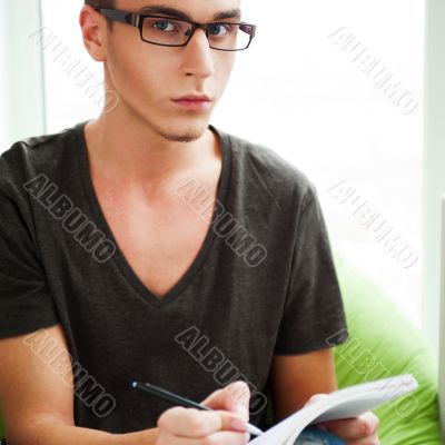 Young adult man writing in his copybook while sitting on a large