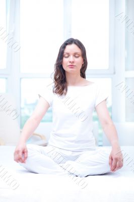 Young woman meditating with closed eyes in bright bedroom sittin