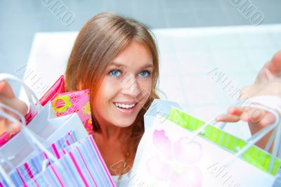 Shopping woman with lots of bags smiles inside mall. She is happ