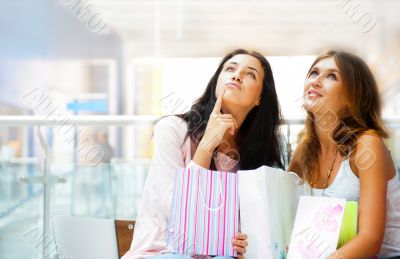 Two excited shopping woman resting on bench at shopping mall. Lo