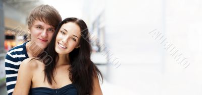 Portrait of young couple embracing at shopping mall and looking 