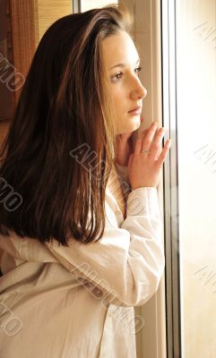 Portrait of cosy young girl standing near a window at home
