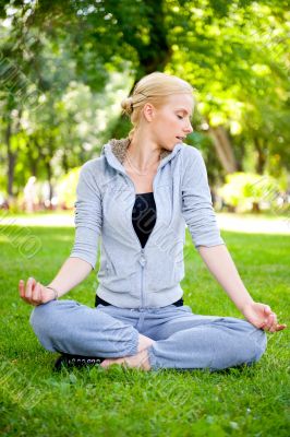 Portrait of young woman meditating in pose of lotus on green gra