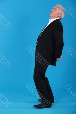 portrait of mature man standing back in profile against blue background