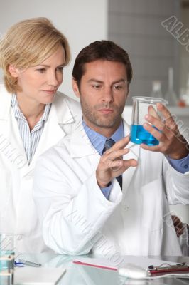 Man and woman in white laboratory coats, examining blue liquid