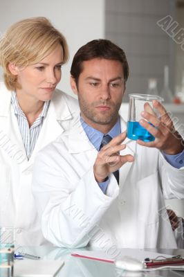 Man and woman in white laboratory coats, examining blue liquid Man and woman in white laboratory coats, examining blue liquid