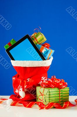 Tablet PC with heap of presents in red bag against blue backgrou Tablet PC with heap of presents in red bag against blue backgrou