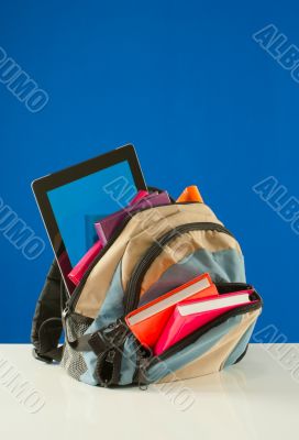 Backpack with colorful books and pablet PC on the blue backgroun