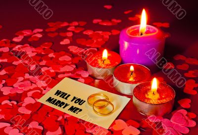 Two rings and a card with marriage proposal with four candles