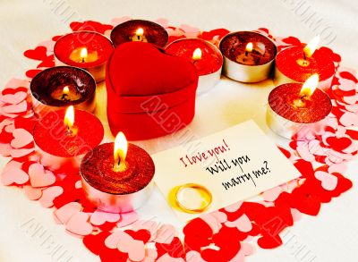 Ring and a card with marriage proposal with candles