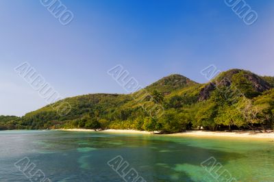 A small turquoise crystal clear tropical beach by hill  