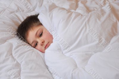 The boy lies in bed covered with a blanket