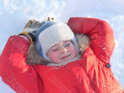 The boy lay on the snow in the bright winter clothes 