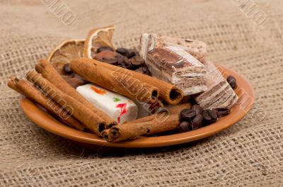 Sweets, cinnamon, nuts and coffee beans on a saucer, on burlap b