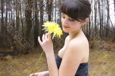 A beautiful woman stands in the forest against the backdrop of nature in a dress with bare shoulders, smiling sweetly and holdin