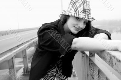 Beautiful woman in a hat and a black shirt, standing on a bridge across the river in foggy weather, and cute smiles