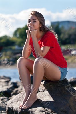 girl in a red sweater sits on a rock