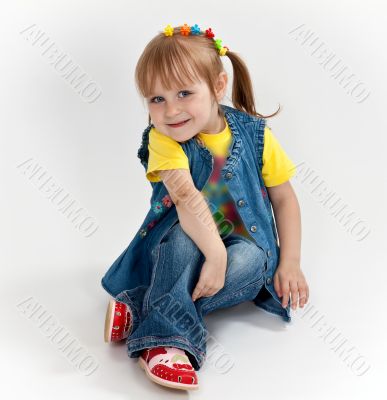 little girl in jeans and sandals is sitting on the floor
