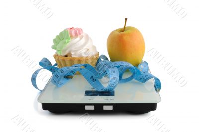 Cake and apple on scales measuring tape wrapped