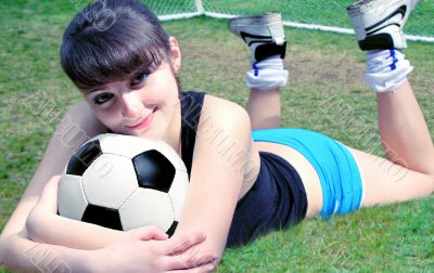 The woman lies on the field with a soccer ball